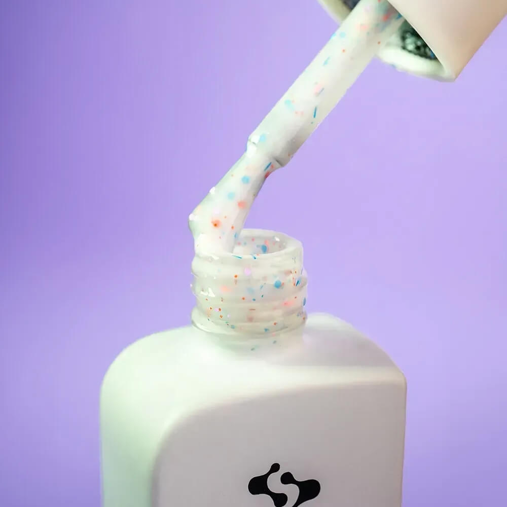 A full set of nails styled with 12ml Inspiration in milky white with rainbow glitter, hand resting on a neutral surface